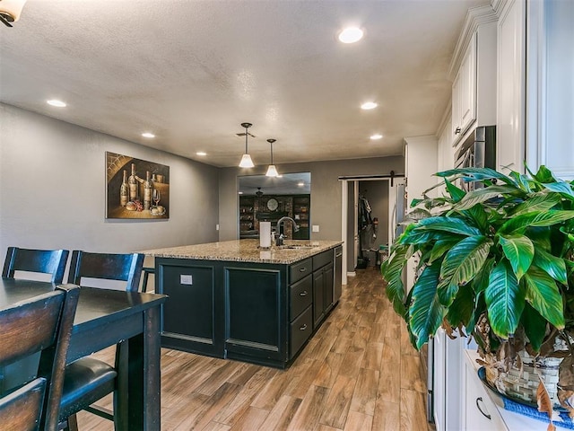 kitchen with sink, white cabinetry, hanging light fixtures, a center island with sink, and a barn door