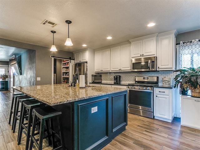 kitchen with stainless steel appliances, white cabinetry, a barn door, and a kitchen island with sink