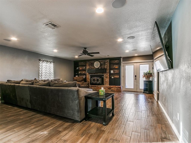 living room featuring ceiling fan, a brick fireplace, hardwood / wood-style floors, and a textured ceiling