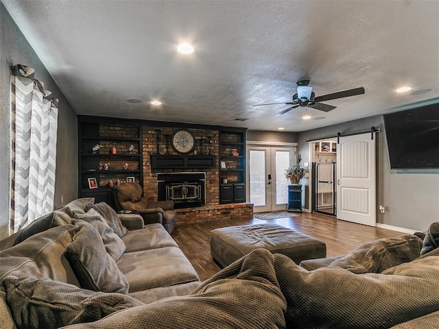 living room with built in features, wood-type flooring, a textured ceiling, french doors, and a barn door