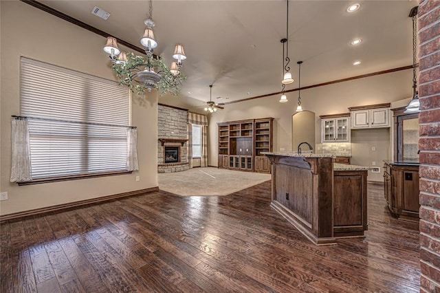 kitchen featuring a stone fireplace, a kitchen island with sink, a kitchen breakfast bar, light stone countertops, and decorative light fixtures