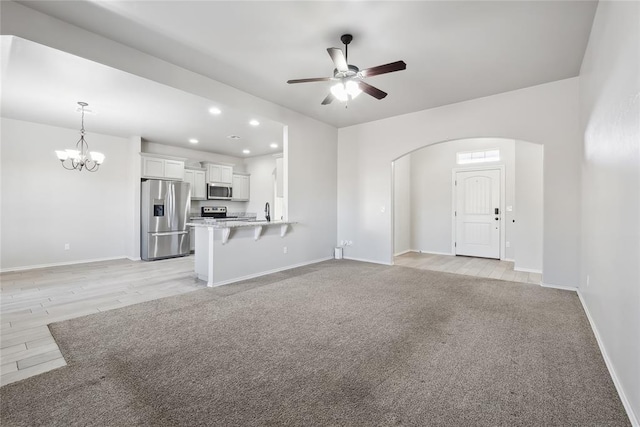 unfurnished living room with light carpet, sink, and ceiling fan with notable chandelier