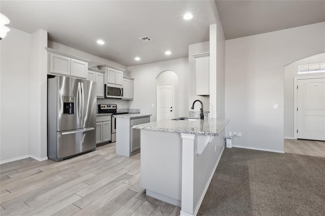 kitchen featuring sink, appliances with stainless steel finishes, light stone counters, a kitchen bar, and kitchen peninsula