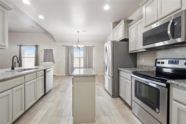 kitchen featuring sink, appliances with stainless steel finishes, light stone countertops, a kitchen island, and decorative light fixtures