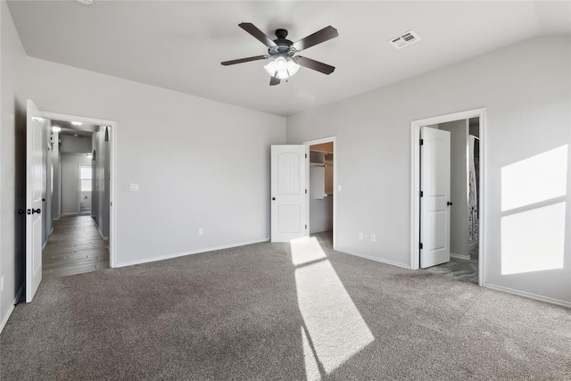 unfurnished bedroom featuring ensuite bathroom, lofted ceiling, a walk in closet, carpet floors, and ceiling fan