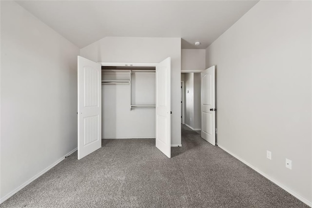 unfurnished bedroom with lofted ceiling, dark carpet, and a closet