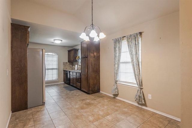 kitchen featuring a notable chandelier, tasteful backsplash, freestanding refrigerator, vaulted ceiling, and dark brown cabinetry