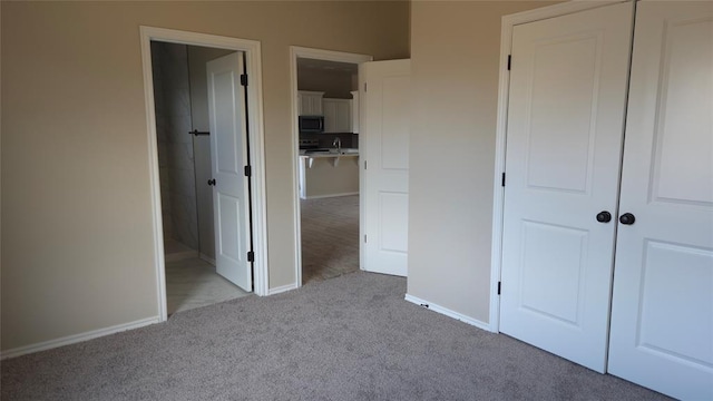 unfurnished bedroom with light carpet, a closet, and ensuite bath