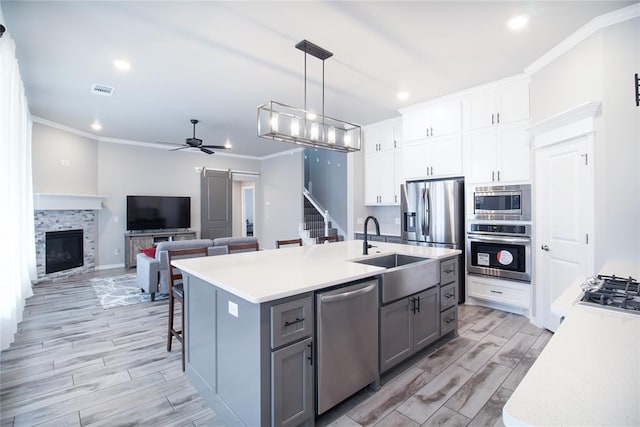 kitchen with sink, appliances with stainless steel finishes, an island with sink, white cabinets, and a barn door