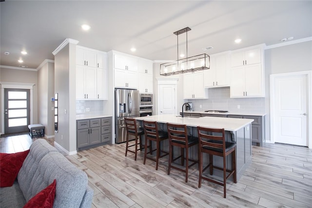 kitchen featuring a breakfast bar area, gray cabinetry, white cabinetry, hanging light fixtures, and stainless steel appliances