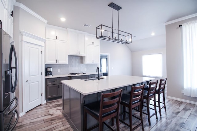 kitchen with pendant lighting, a kitchen island with sink, stainless steel fridge with ice dispenser, and white cabinets