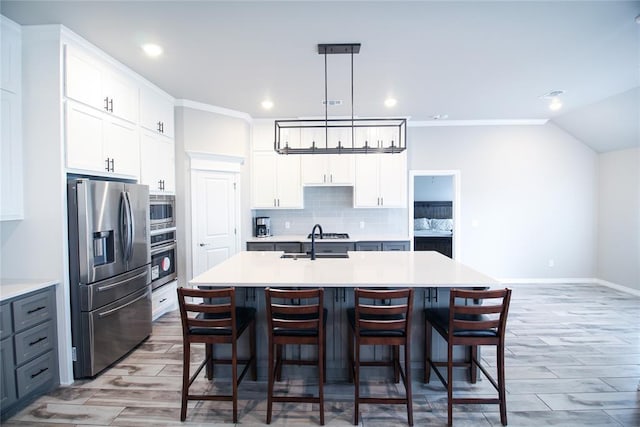 kitchen featuring appliances with stainless steel finishes, tasteful backsplash, white cabinetry, hanging light fixtures, and a center island with sink