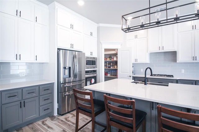 kitchen featuring a breakfast bar, hanging light fixtures, stainless steel appliances, decorative backsplash, and white cabinets