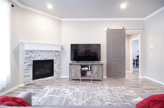 living room with ornamental molding, a barn door, light hardwood / wood-style floors, and a stone fireplace