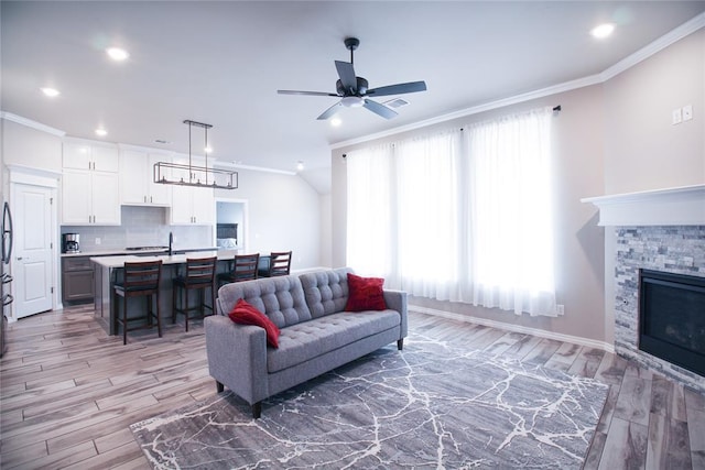 living room with ceiling fan, ornamental molding, a stone fireplace, and hardwood / wood-style floors