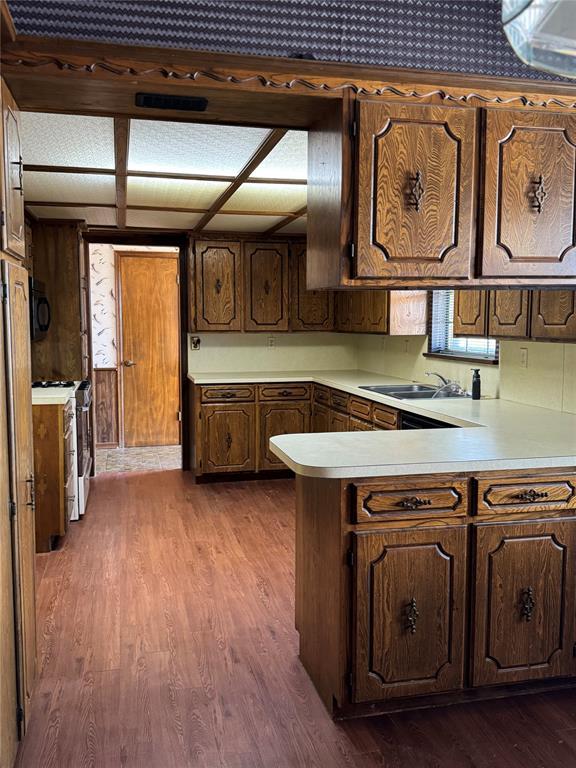 kitchen with sink, stainless steel stove, dark brown cabinets, dark hardwood / wood-style floors, and kitchen peninsula