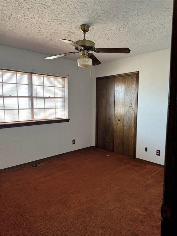 unfurnished bedroom featuring dark colored carpet, ceiling fan, a textured ceiling, and a closet