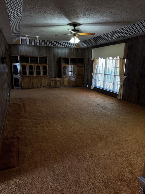 unfurnished living room featuring ceiling fan, carpet flooring, a textured ceiling, and wood walls