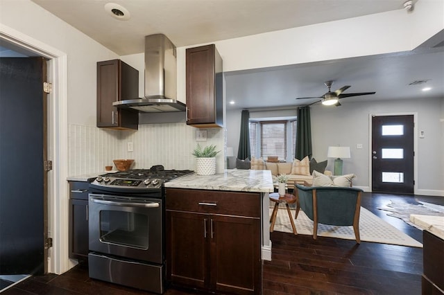 kitchen featuring wall chimney exhaust hood, gas stove, tasteful backsplash, dark brown cabinets, and dark hardwood / wood-style flooring