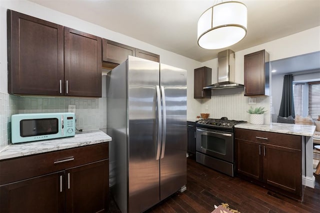 kitchen featuring wall chimney exhaust hood, dark brown cabinetry, appliances with stainless steel finishes, dark hardwood / wood-style floors, and light stone countertops