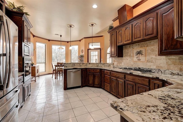 kitchen featuring sink, light stone counters, decorative light fixtures, appliances with stainless steel finishes, and kitchen peninsula