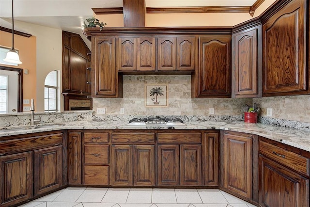 kitchen with light tile patterned flooring, sink, hanging light fixtures, stainless steel gas stovetop, and light stone countertops