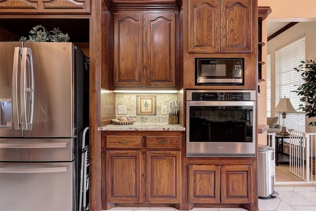 kitchen featuring tasteful backsplash, crown molding, light tile patterned floors, appliances with stainless steel finishes, and light stone countertops