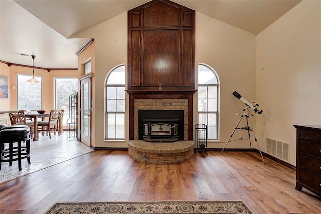 living room with ornamental molding, vaulted ceiling, light hardwood / wood-style flooring, and a wood stove