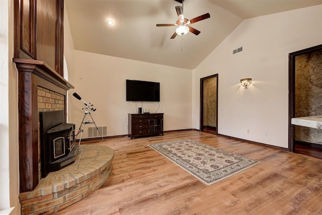 living room with ceiling fan, high vaulted ceiling, light hardwood / wood-style floors, and a wood stove