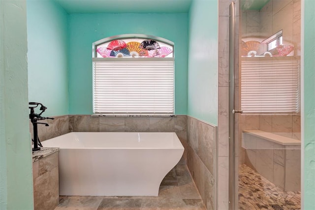 bathroom with tile walls, a wealth of natural light, and independent shower and bath