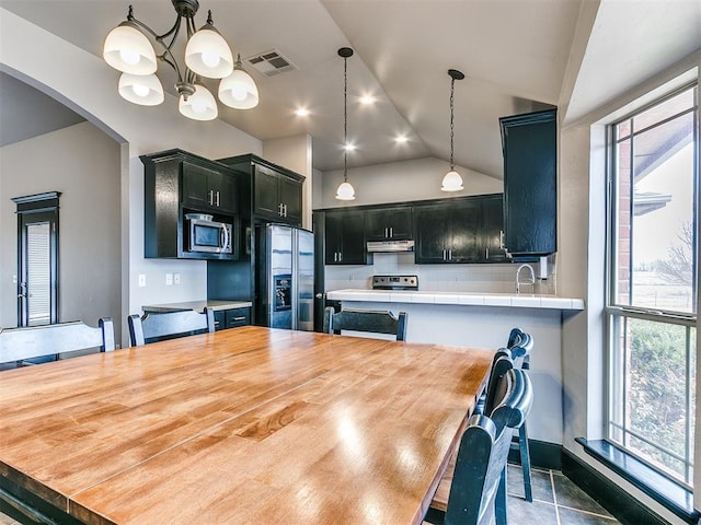 kitchen with lofted ceiling, decorative light fixtures, plenty of natural light, and stainless steel appliances