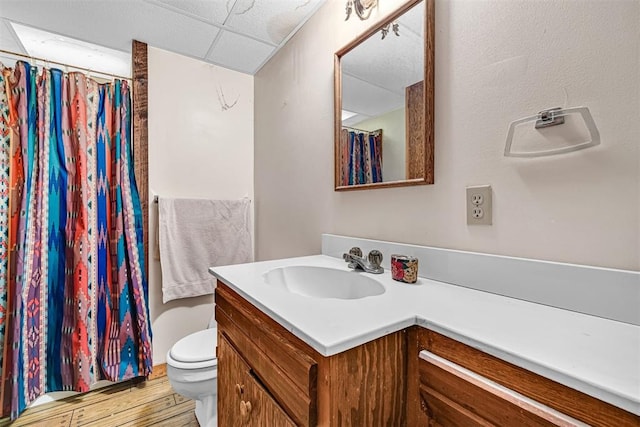 bathroom with vanity, toilet, wood-type flooring, and a drop ceiling