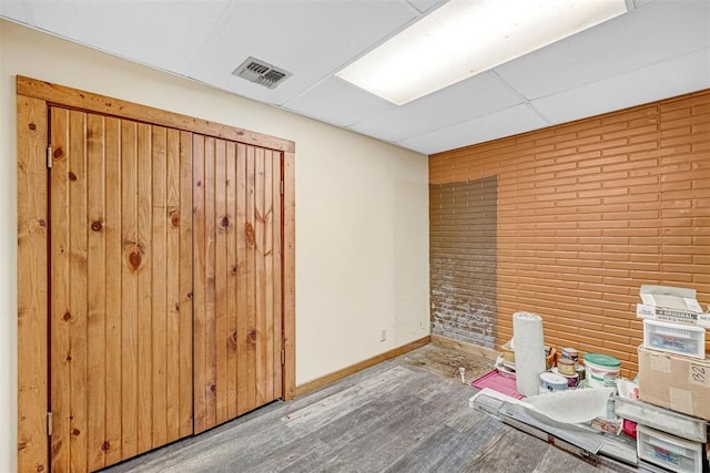 unfurnished office with hardwood / wood-style flooring, brick wall, and a drop ceiling