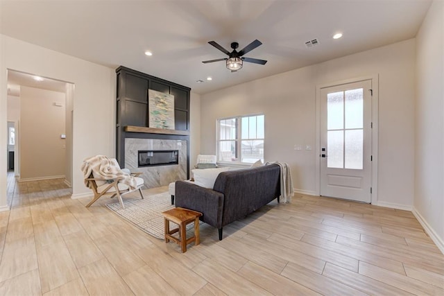 living room featuring ceiling fan, a premium fireplace, and light wood-type flooring