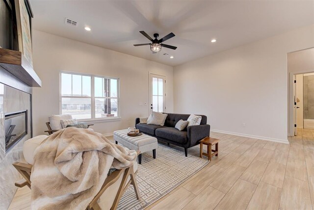 living room featuring ceiling fan, a tile fireplace, and light hardwood / wood-style flooring