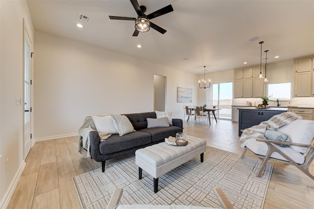 living room with sink, ceiling fan with notable chandelier, and light hardwood / wood-style floors