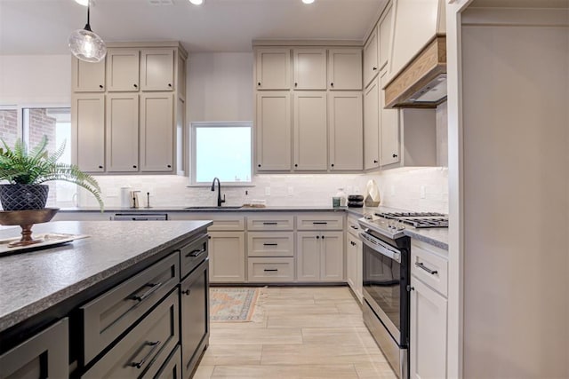 kitchen featuring gas range, decorative backsplash, sink, and hanging light fixtures