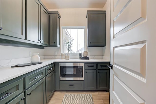 kitchen featuring stainless steel microwave, light stone counters, and light hardwood / wood-style flooring