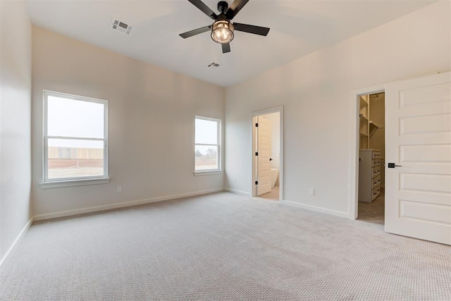 unfurnished bedroom featuring connected bathroom, a walk in closet, light colored carpet, a closet, and ceiling fan