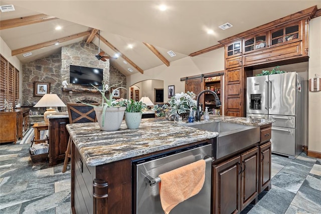 kitchen with sink, beam ceiling, appliances with stainless steel finishes, a barn door, and a kitchen island with sink