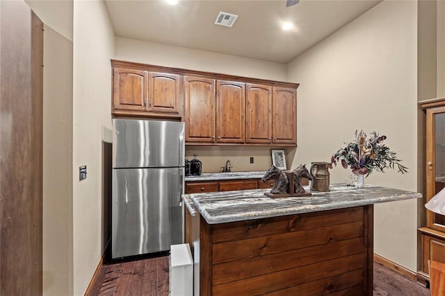 kitchen with dark hardwood / wood-style floors, stainless steel fridge, light stone countertops, and sink