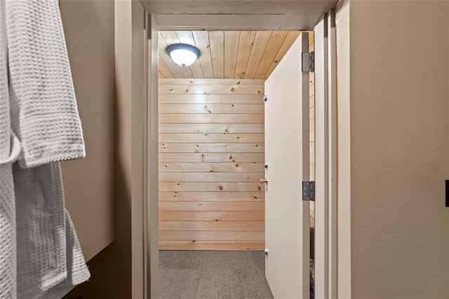 hall with wood ceiling, wood walls, and carpet flooring