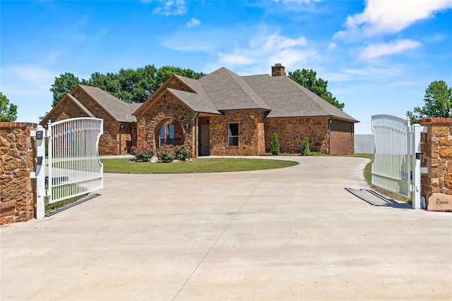 french country home featuring a gate, stone siding, a chimney, and a front yard