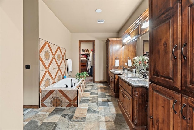 full bath with a garden tub, vanity, a spacious closet, baseboards, and stone finish flooring