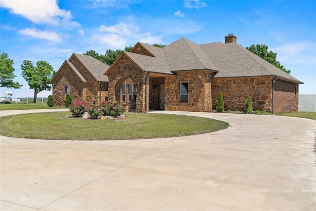 french country style house featuring curved driveway, a front lawn, stone siding, and a chimney