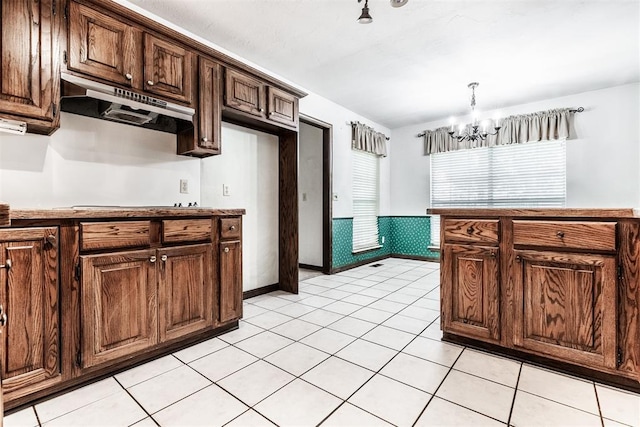 kitchen featuring stovetop, dark brown cabinets, light tile patterned floors, hanging light fixtures, and a notable chandelier