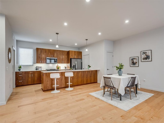 kitchen featuring tasteful backsplash, stainless steel appliances, hanging light fixtures, and light wood-type flooring