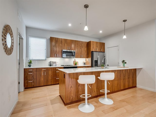 kitchen with sink, pendant lighting, stainless steel appliances, light hardwood / wood-style floors, and decorative backsplash