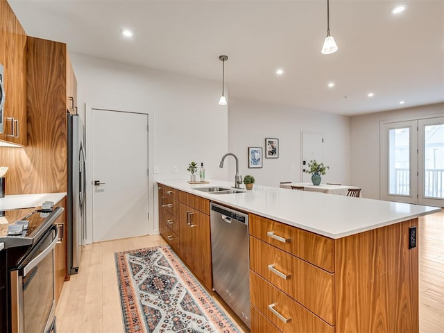 kitchen with appliances with stainless steel finishes, decorative light fixtures, sink, a kitchen island with sink, and light wood-type flooring