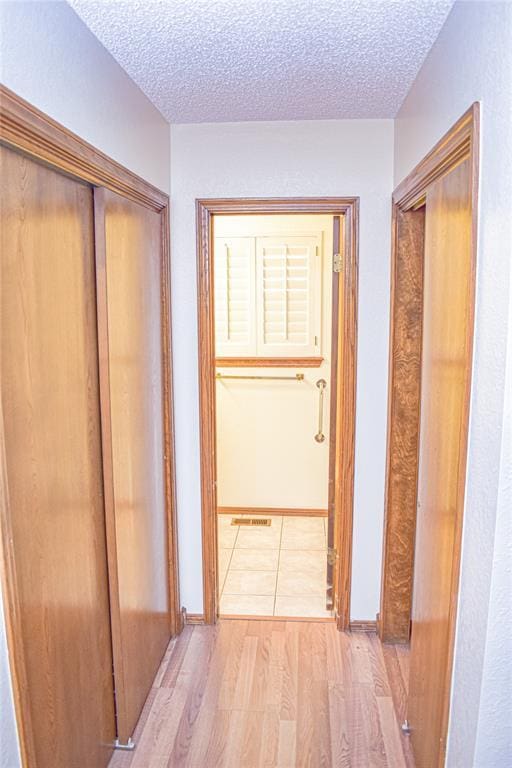 hall with a textured ceiling and light wood-type flooring